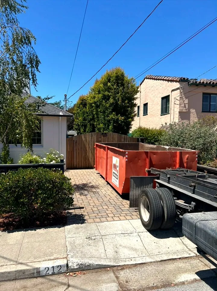 Orange Mosso roll-off dumpster set on a paver driveway beside the truck