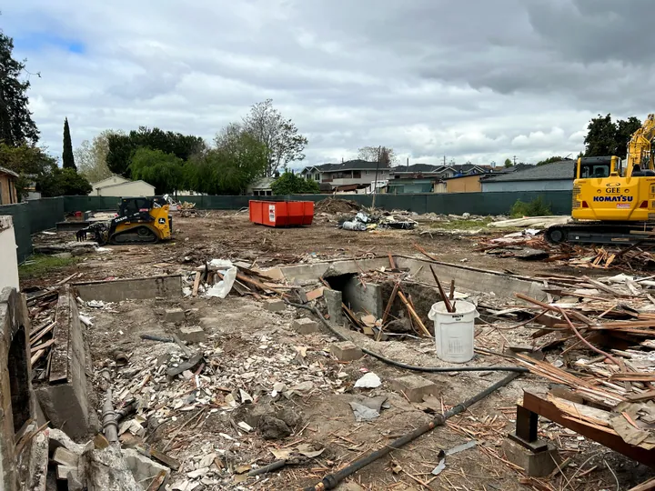 Cleared house foundation with excavator and roll-off on site