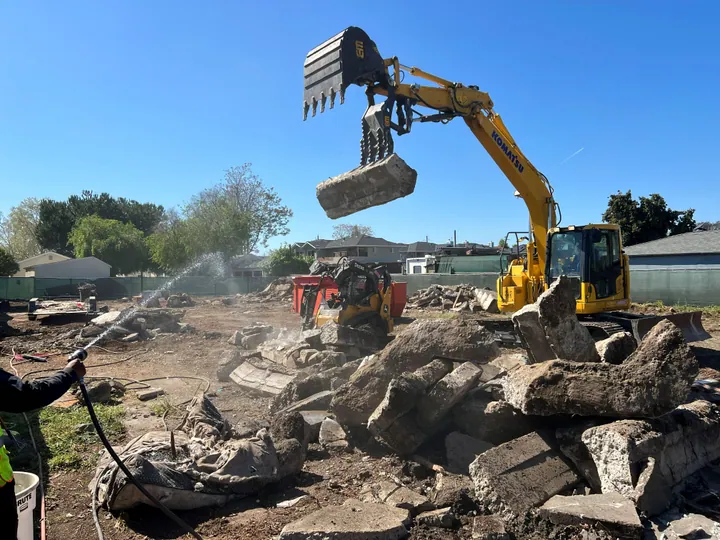 Excavator grapple sorting concrete rubble with water spray