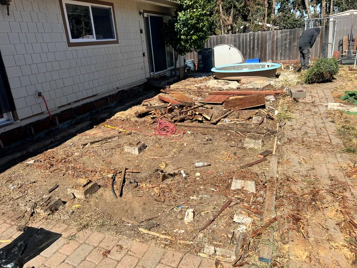 Backyard with the deck torn out and the old hot tub lifted clear, debris ready to haul