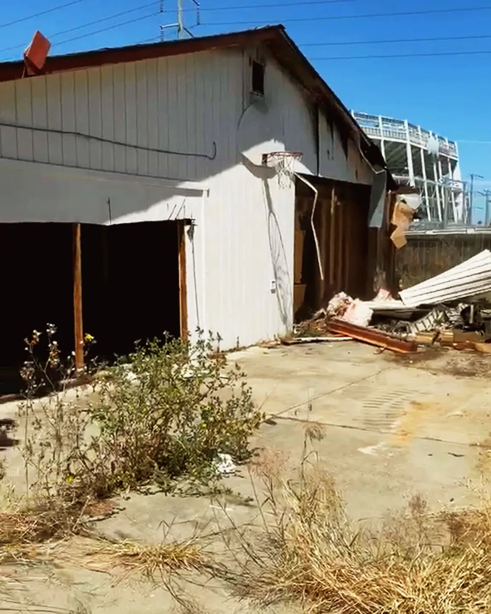 Before: overgrown lot with an old white garage building still standing, Levi's Stadium behind it
