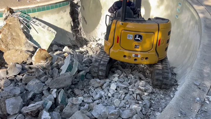 Mosso excavator inside a swimming pool shell, broken concrete and rebar around it
