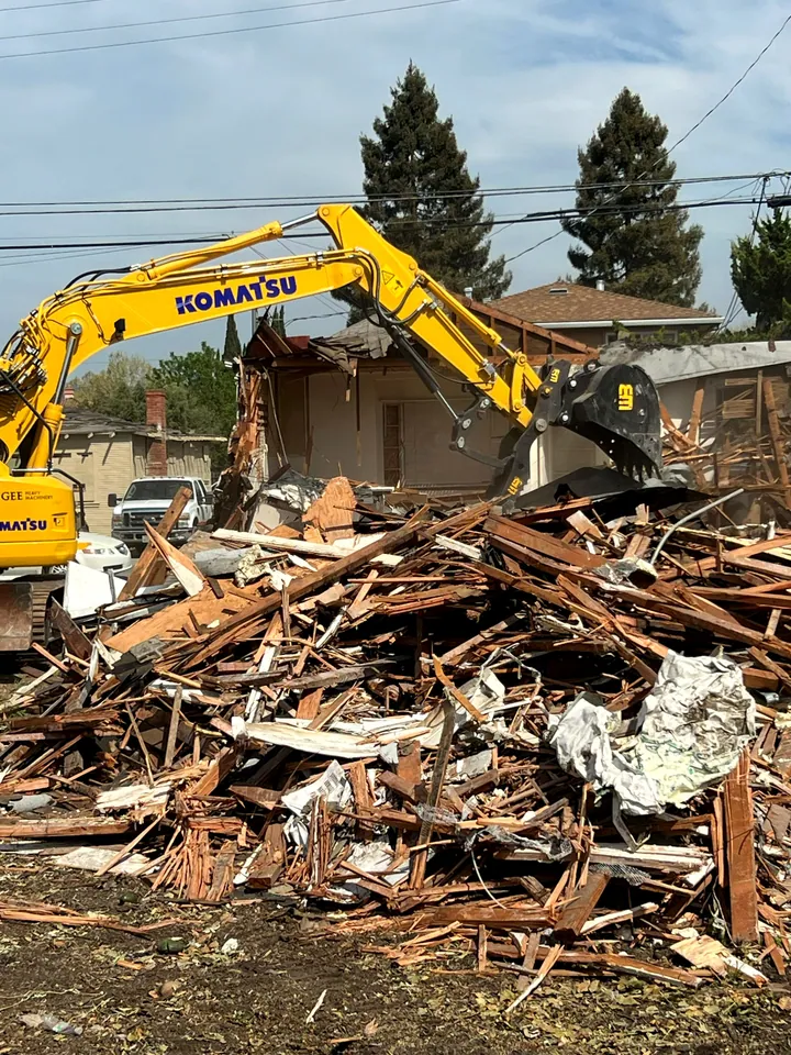 Komatsu excavator beside the debris pile of a torn-down house